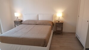 A neatly made bed with a beige blanket, two bedside tables with lamps, and a wardrobe. - La Coffa (Noto)