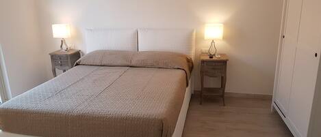 A neatly made bed with a beige blanket, two bedside tables with lamps, and a wardrobe.