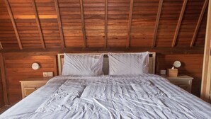 A wooden ceiling with exposed beams, a bed with white bedding, two bedside tables, and a wall-mounted light fixture. - Plumeria NP (Penida Island)