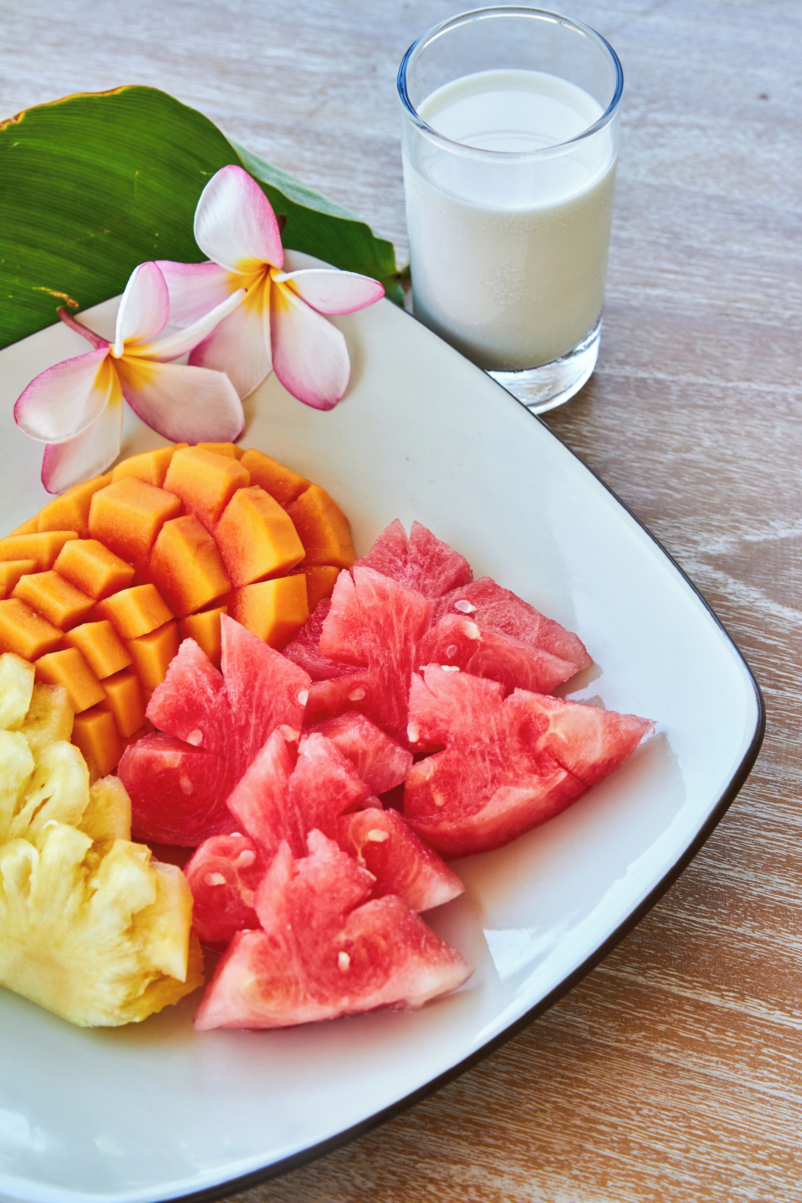 A plate with sliced mango, watermelon, pineapple, and a glass of milk.