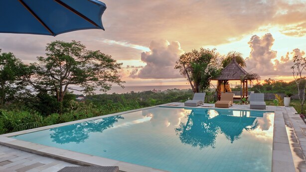 A swimming pool with lounge chairs and a gazebo, surrounded by greenery and a sunset view. - Plumeria NP (Penida Island)