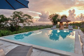 A swimming pool with lounge chairs and a gazebo, surrounded by greenery and a sunset view. - Plumeria NP (Penida Island)