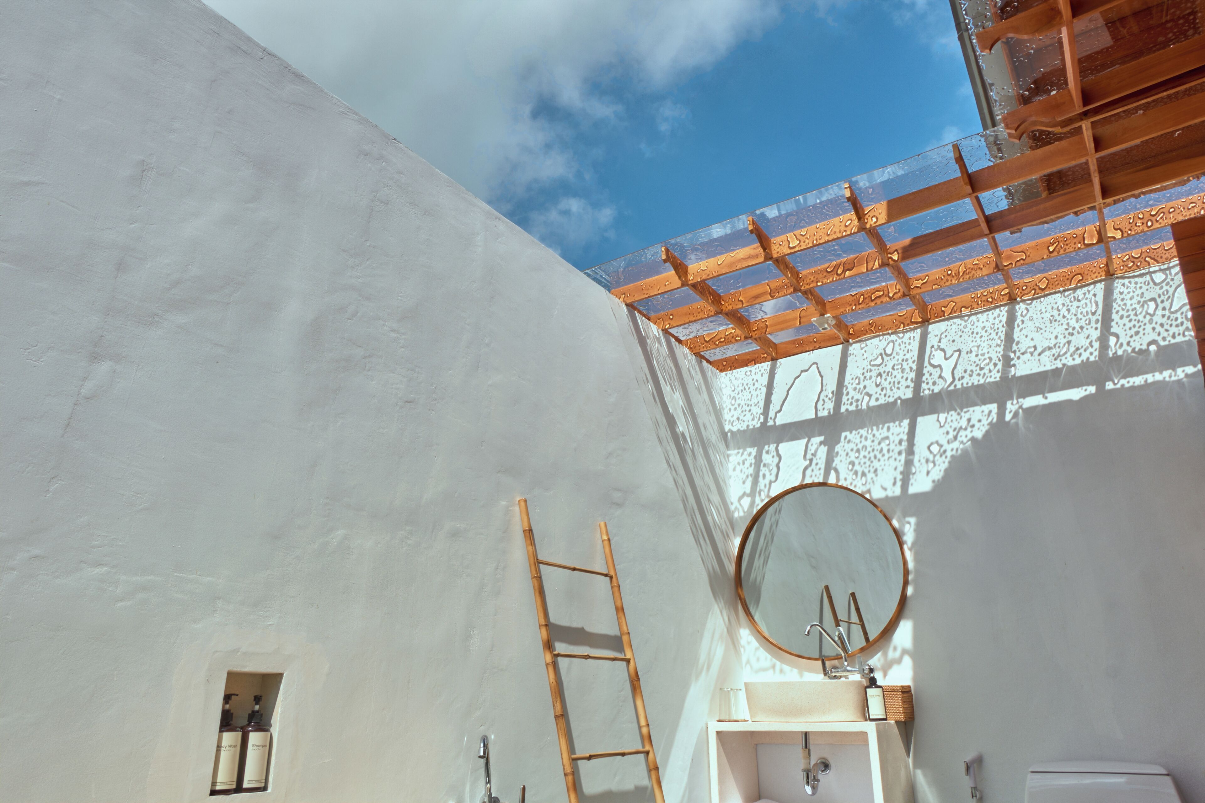 A bathroom with a white wall, a wooden ladder, a round mirror, and a window with a wooden frame.