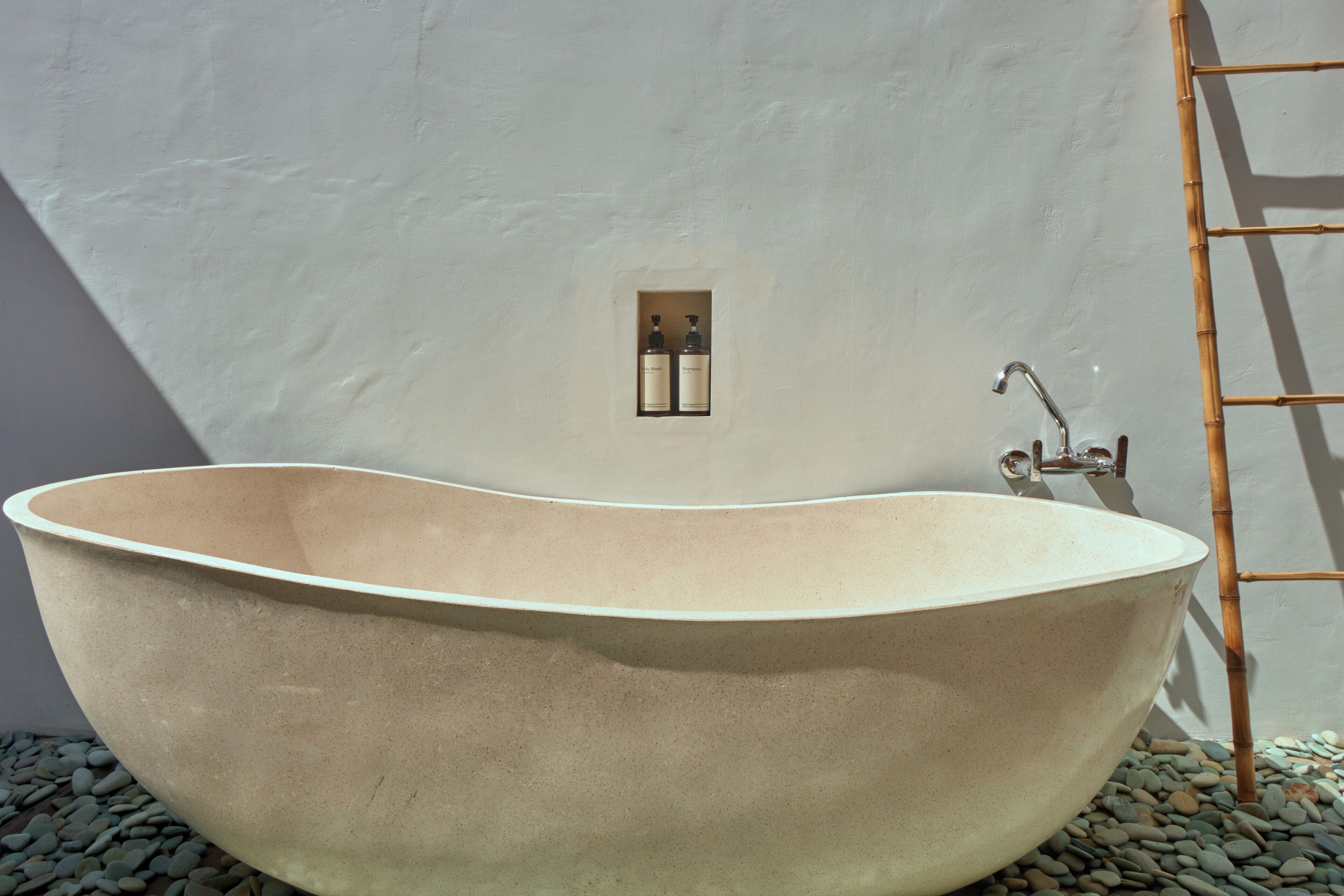 A freestanding bathtub in a bathroom with a white wall, a small window, and a bamboo ladder.
