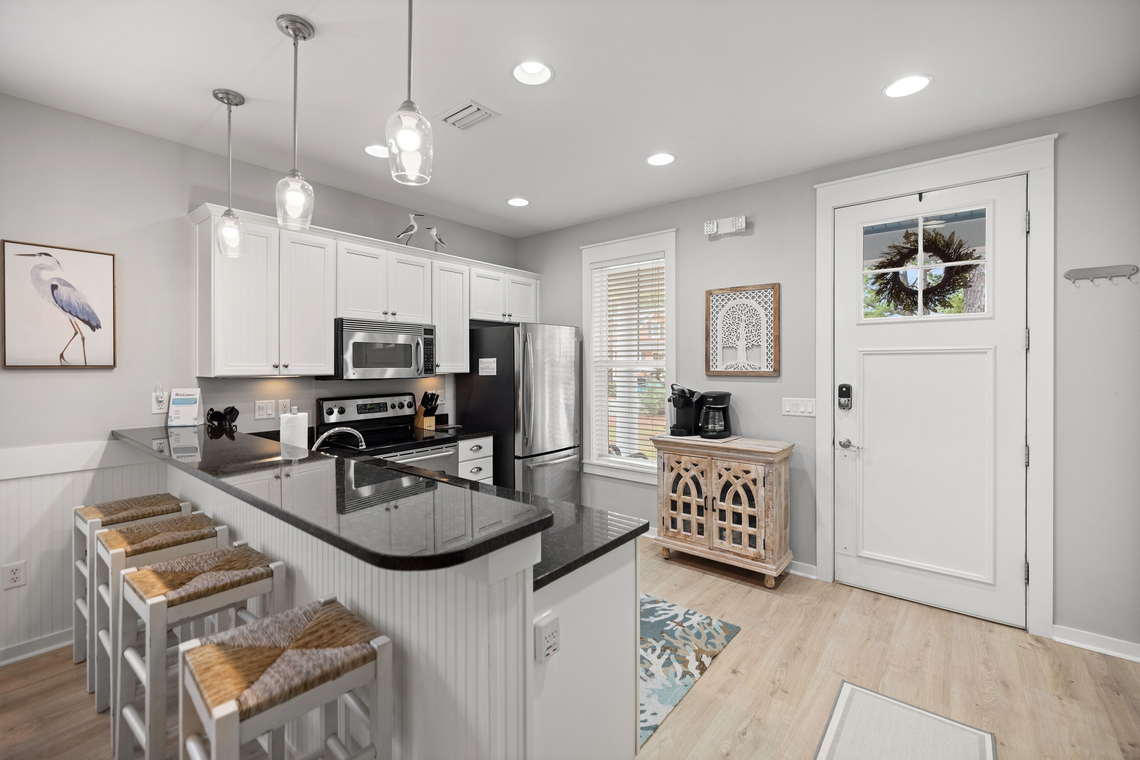 A modern kitchen with white cabinetry, a central island with stools, stainless steel appliances, and pendant lighting.