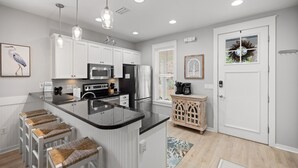 A modern kitchen with white cabinetry, a central island with stools, stainless steel appliances, and pendant lighting. - 1298 Laurel Grove 3 Bedroom Home by RedAwning (Miramar Beach)