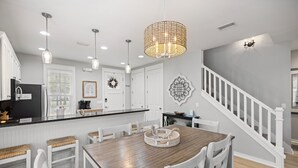 A modern kitchen with white cabinetry, a wooden dining table, and a staircase. - 1298 Laurel Grove 3 Bedroom Home by RedAwning (Miramar Beach)