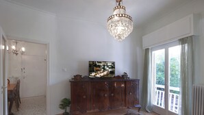 A living room with a wooden cabinet, a glass coffee table, a chandelier, and a television. - Neasefessou25 (Kaisariani)