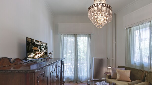 A modern living room with a wooden cabinet, a glass coffee table, a sofa, and a chandelier. - Neasefessou25 (Kaisariani)