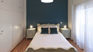 A bedroom with a large bed, two bedside tables with lamps, a wardrobe, and a window with curtains. - Neasefessou25 (Kaisariani)