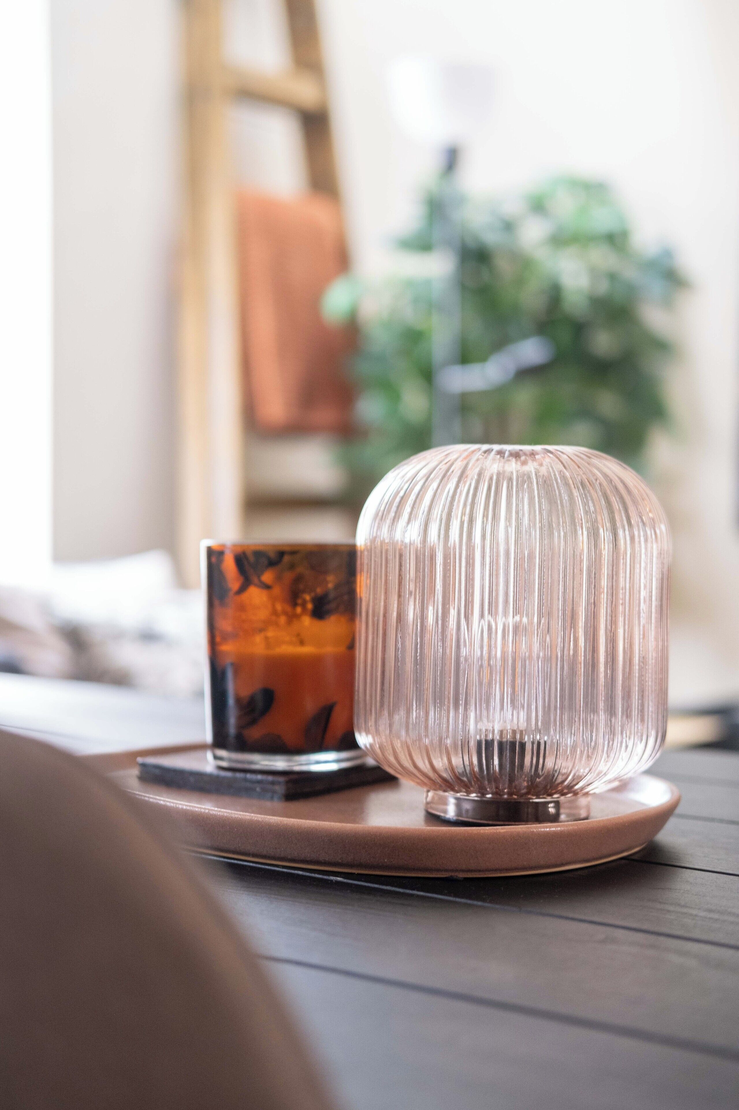 Une table en bois, avec un verre et un porte-bougie en verre à motifs.