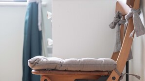 Een houten klapstoel met kussen, voor een witte kast geplaatst.