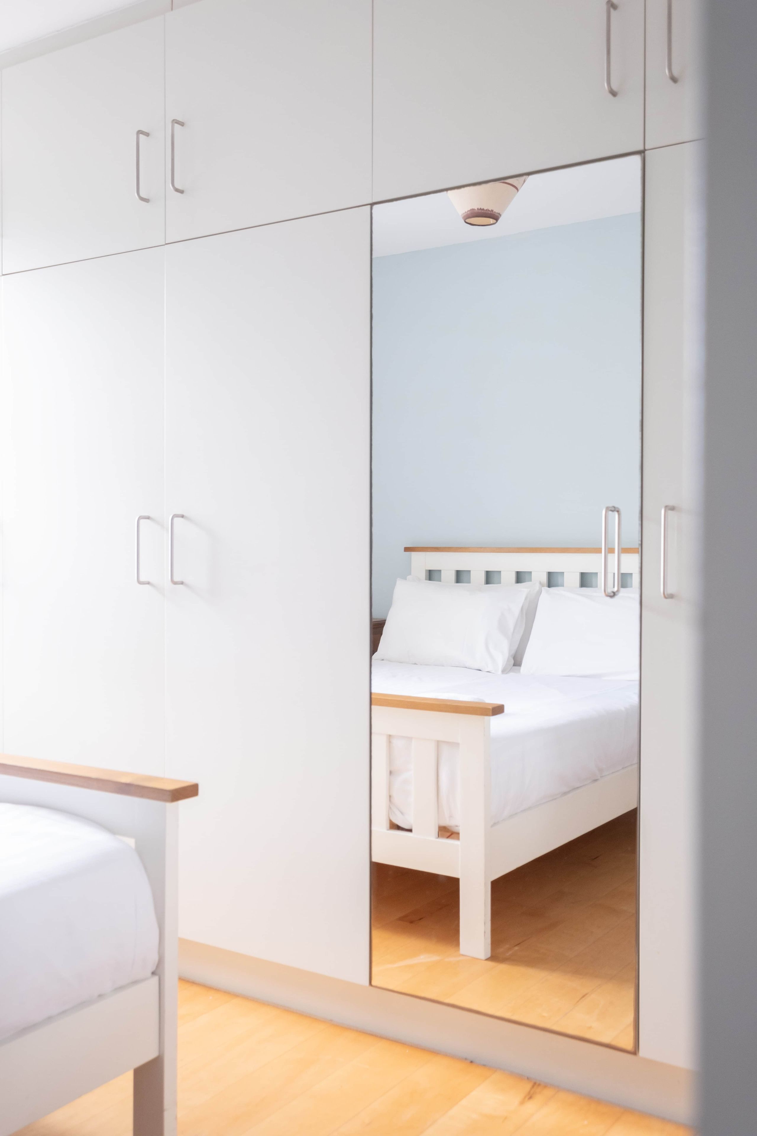 A bedroom with a bed, white wardrobe, and a mirror reflecting the bed.