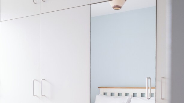 Une chambre à coucher avec un lit, une armoire blanche et un miroir qui reflète la pièce.