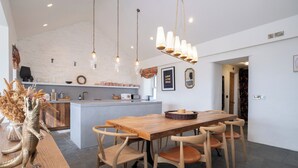 Una cucina moderna con isola in legno, illuminazione a sospensione e zona pranzo con sedie e tavolo in legno.