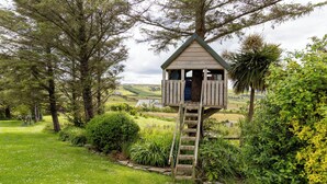 Uma casa na árvore de madeira com uma escada, rodeada por vegetação exuberante e uma paisagem deslumbrante.