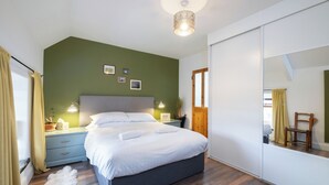 Quarto com cama, mesas de cabeceira, espelho e vista para uma cadeira pela janela.
