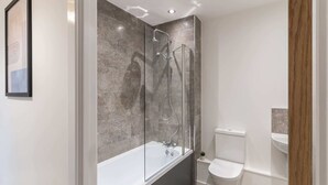 Ein modernes Badezimmer mit einer gläsernen Duschkabine, einer weißen Badewanne und einem WC.