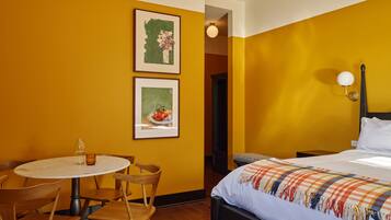 A hotel room with a bed, a round table with chairs, and two framed pictures on the wall.
