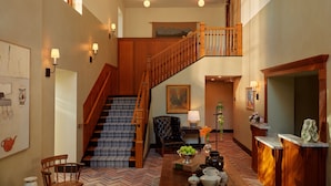 A spacious foyer with a wooden staircase, a reception desk, and a seating area. - The Abner Hotel (Litchfield)