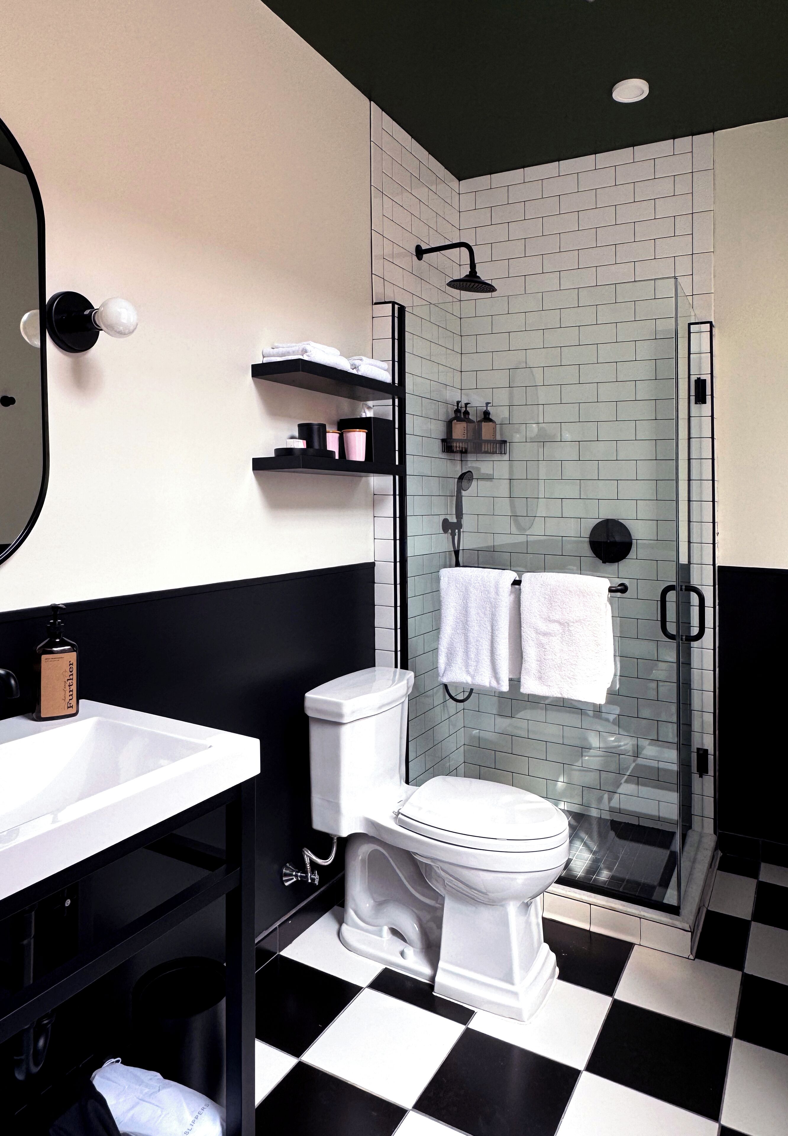 A bathroom with a black and white checkered floor, a white toilet, a glass-enclosed shower, and a black sink with a mirror above it.