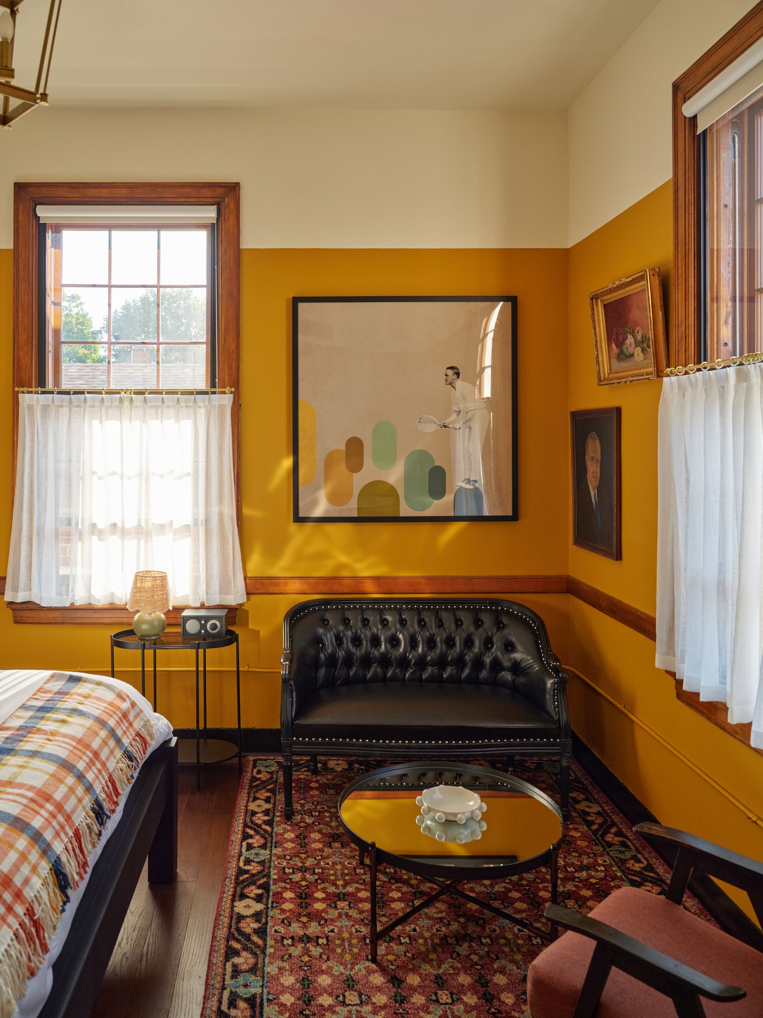 A room with a bed, a black leather sofa, a small table, a rug, and a painting on the wall.