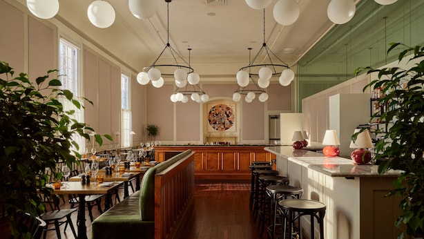 A restaurant with wooden tables and chairs, a bar area, and hanging spherical light fixtures. - The Abner Hotel (Litchfield)