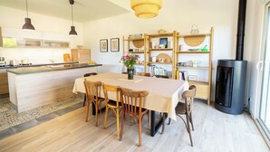 Una cocina moderna con una isla central, sillas de madera, una mesa de comedor, luces colgantes, una estantería y una estufa negra.