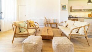 Un salón luminoso con muebles de mimbre, una mesa de centro de madera y vistas a la cocina.