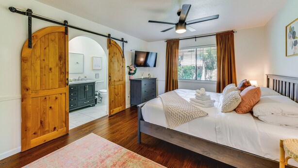Une chambre à coucher avec un lit, un téléviseur, une porte en bois et une vue sur l’extérieur.