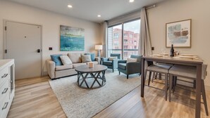 A modern living room with a sofa, chairs, a coffee table, and a dining table set for two. - Walk Everywhere! Central Traverse City Condo (Traverse City)