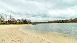 A sandy beach with a calm lake, a small building, and leafless trees in the background. - Lovely Tobyhanna Getaway, Close to Everything (Tobyhanna)