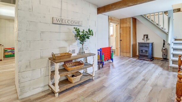 A rustic interior with a 'WELCOME' sign, a wooden table with baskets, a plant, and a staircase leading to a loft. - Lovely Tobyhanna Getaway, Close to Everything (Tobyhanna)