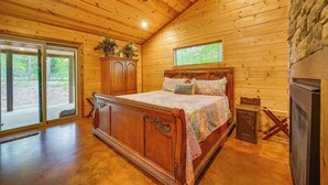 A wooden cabin bedroom with a large bed, a ceiling fan, a window, and a refrigerator. - Broken Bow Cabin: Hot Tub, Fire Pit & 7 Mi to Lake (Broken Bow)
