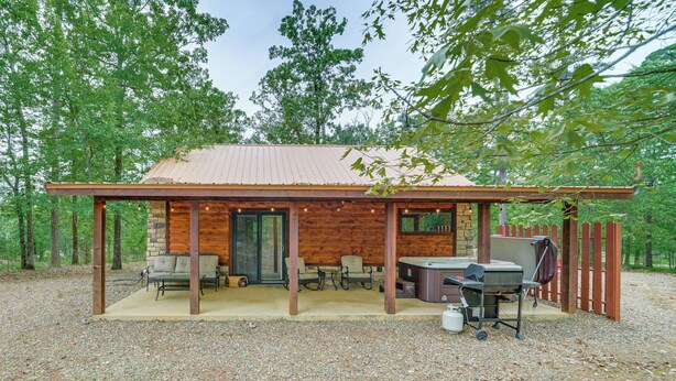 A rustic cabin with a covered patio, stone walls, and a grill area. - Broken Bow Cabin: Hot Tub, Fire Pit & 7 Mi to Lake (Broken Bow)