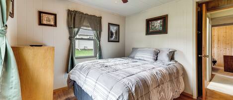 Un dormitorio con cama, piso de madera, ventilador de techo y una puerta que da a otra habitación.