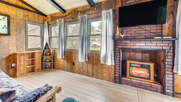 A cozy cabin with a wooden interior, a fireplace, a television mounted above it, and a bed with a patterned bedspread. - Charming Spirit Lake Home - 6 Mi to Arnolds Park! (Spirit Lake)