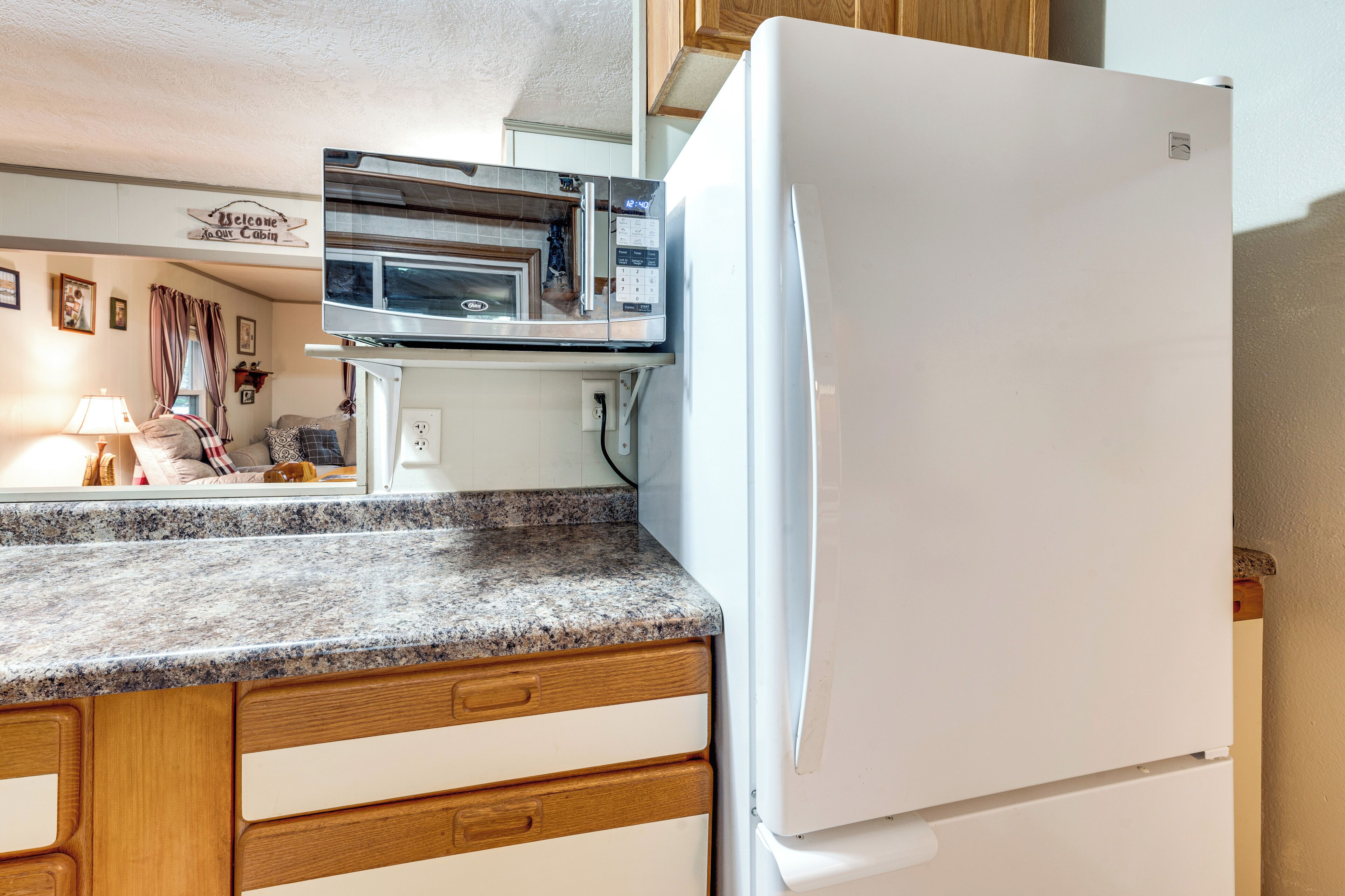 A kitchen with a built-in microwave, a white refrigerator, wooden cabinets, and a granite countertop.