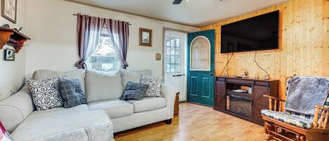 A cozy living room with a sofa, a wooden chair, a fireplace, and a TV mounted on the wall.