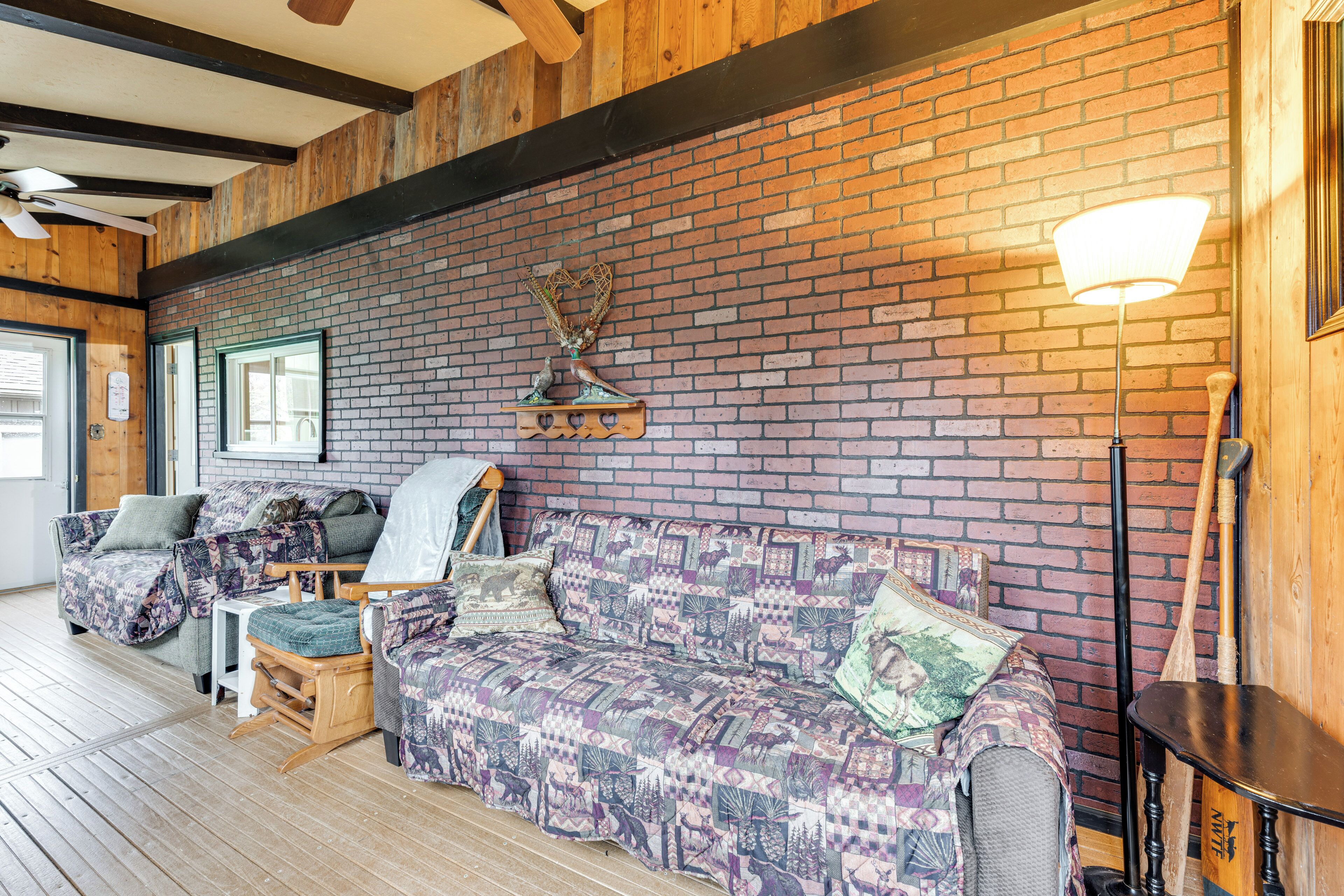 A cozy room with a brick wall, wooden beams, a patterned sofa, a small table, and a lamp.