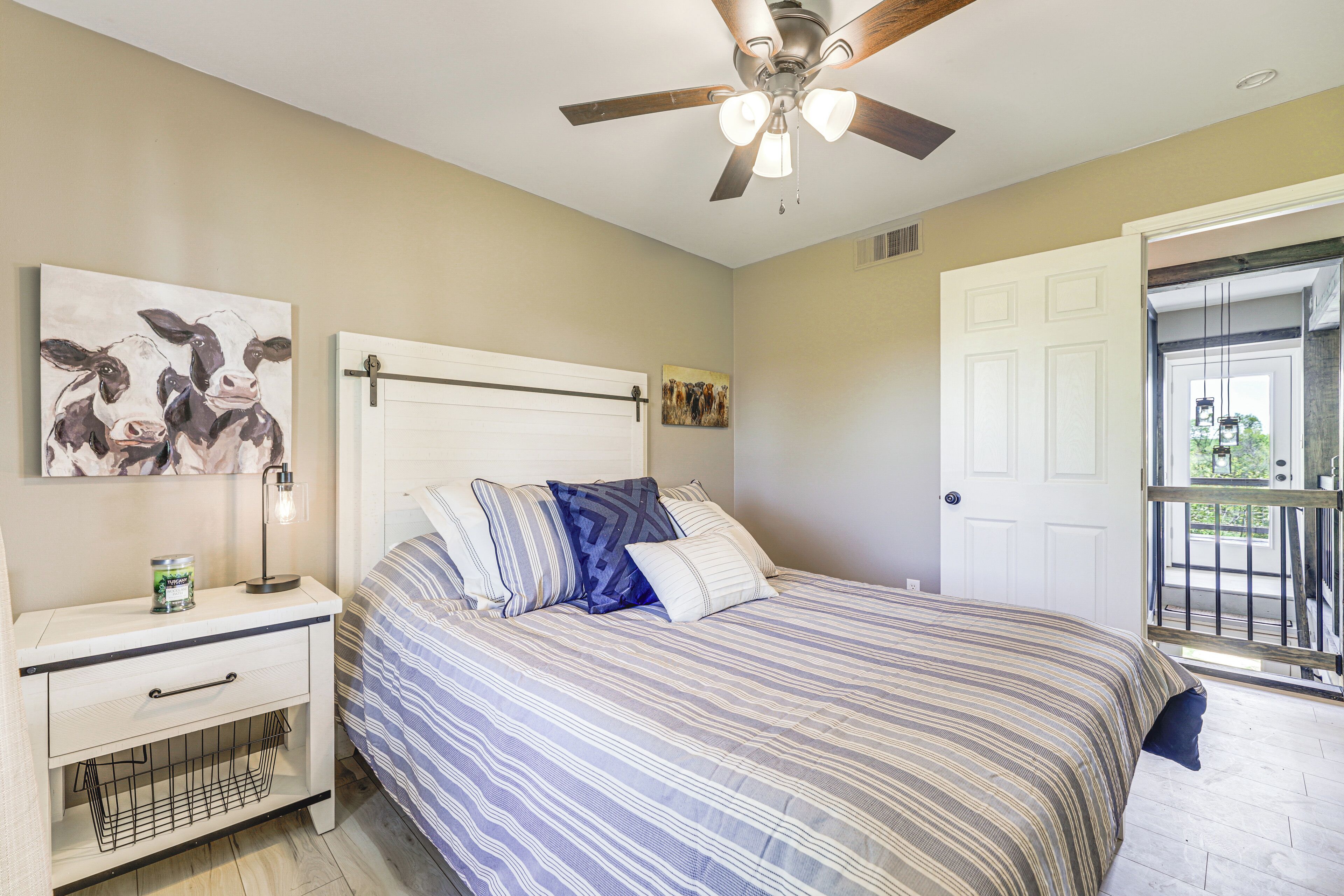 A bedroom with a bed, a nightstand, a ceiling fan, and a door leading to a balcony.