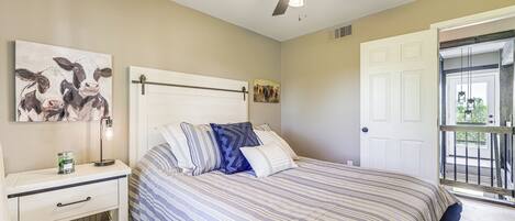 A bedroom with a bed, a nightstand, a ceiling fan, and a door leading to a balcony.