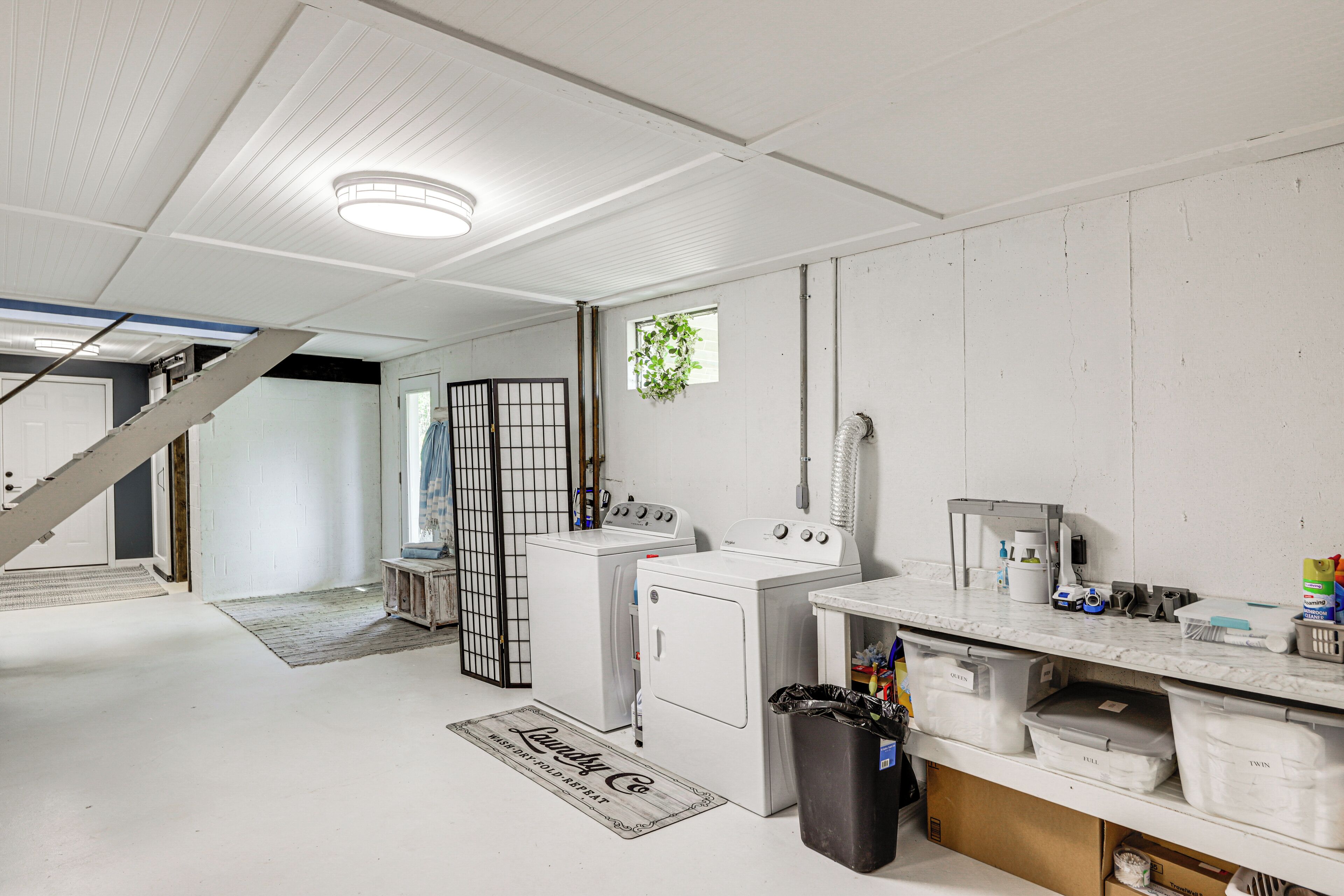 A laundry room with stacked washer and dryer, a trash can, and a countertop with cleaning supplies.