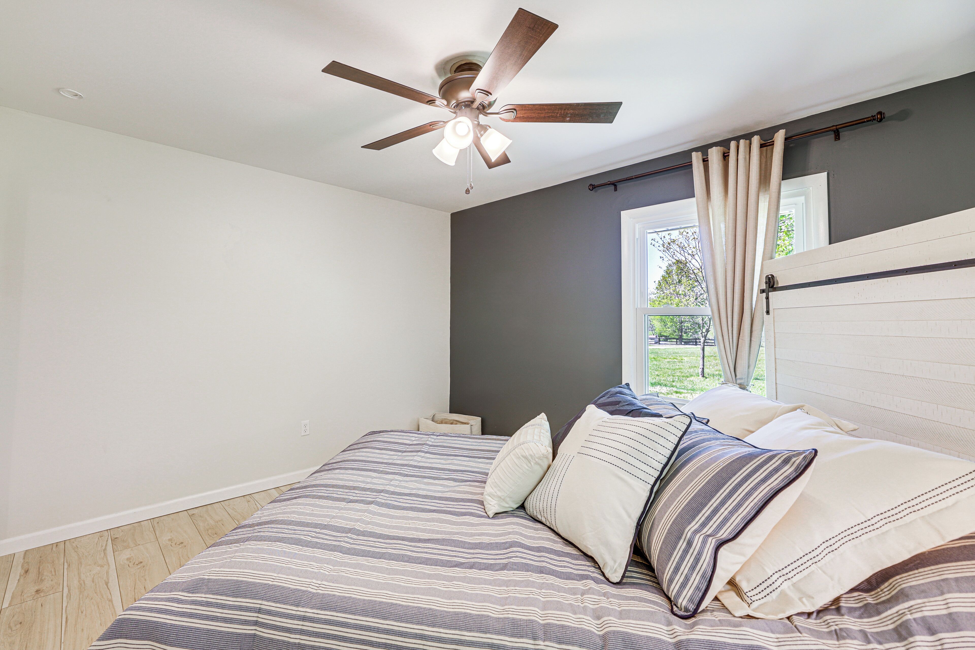 A bedroom with a bed, a ceiling fan, a window with curtains, and a nightstand.