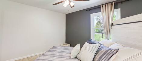 A bedroom with a bed, a ceiling fan, a window with curtains, and a nightstand.