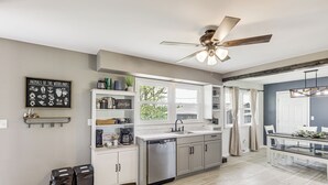 A modern kitchen with a dishwasher, a coffee station, and a dining area with a glass table. - Dry Ridge Farmhouse w/ Hot Tub + Game Room! (Dry Ridge)