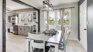 A modern kitchen with white cabinets, a built-in dishwasher, and a dining area with a wooden table and white chairs. - Dry Ridge Farmhouse w/ Hot Tub + Game Room! (Dry Ridge)