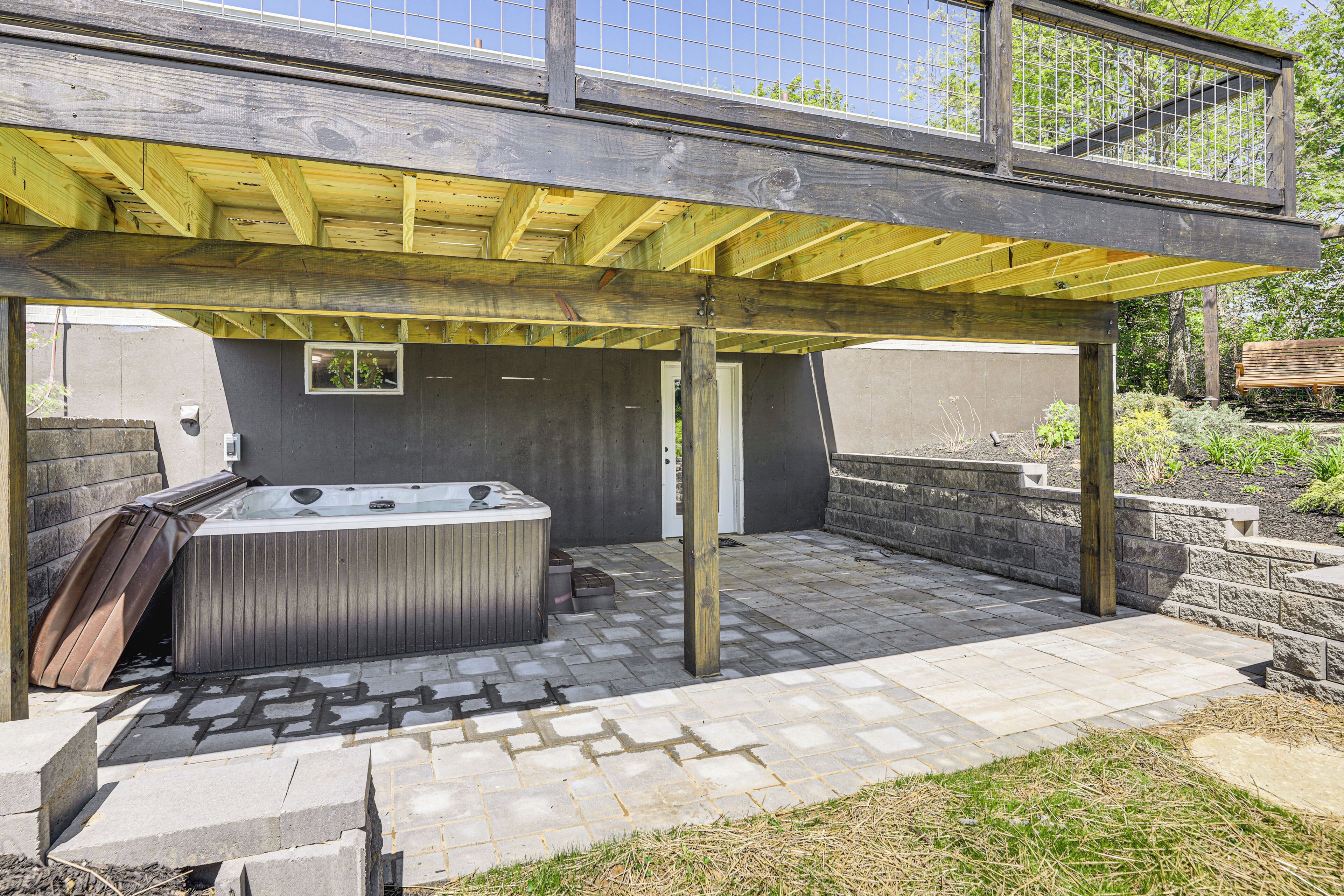 A covered outdoor patio with a hot tub, stone flooring, and a wooden pergola structure.