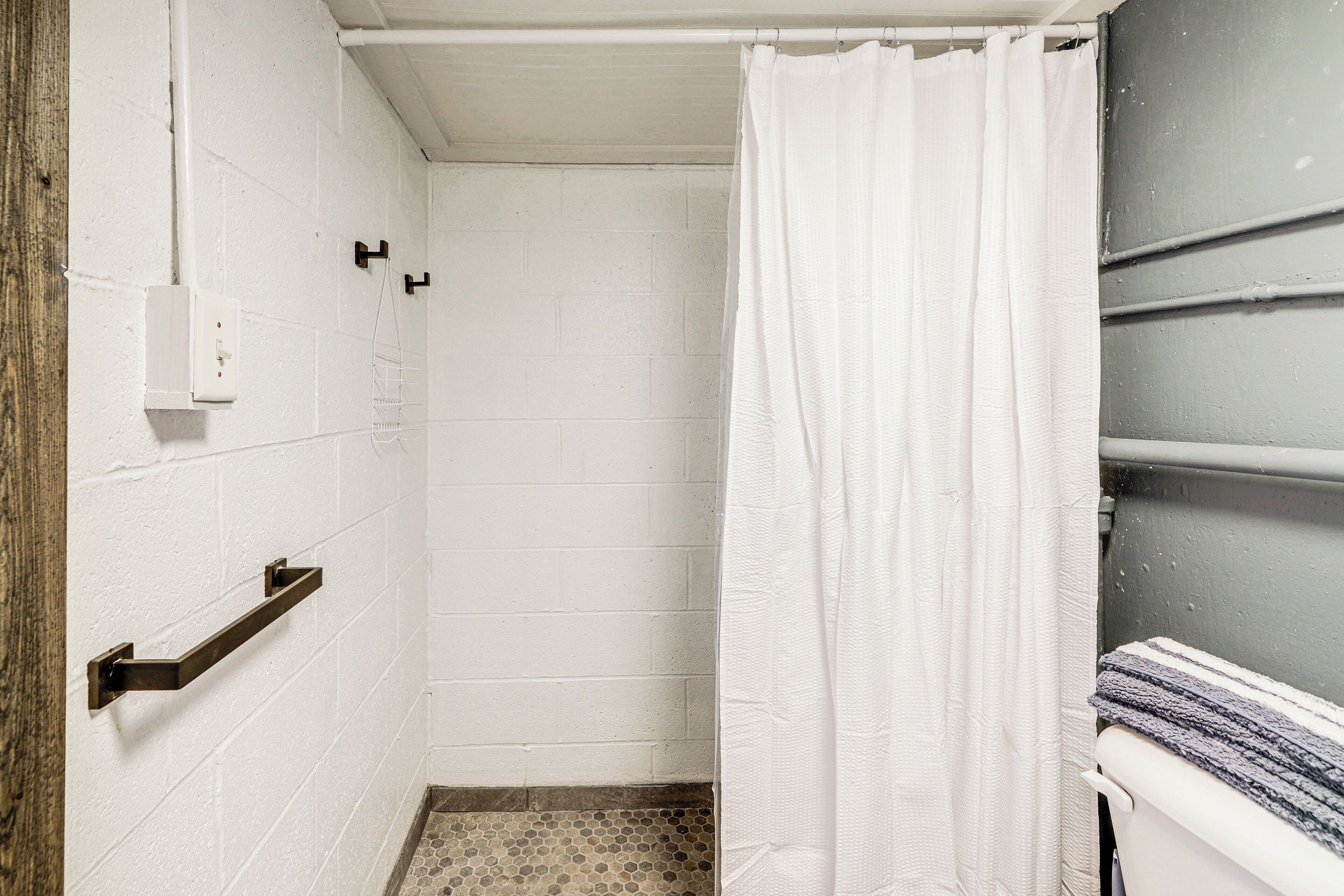 A small, white-walled bathroom with a shower curtain, a towel rack, and a tiled floor.