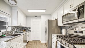 A modern kitchen with white cabinets, a stainless steel refrigerator, a microwave, and a gas stove. - Indiana Dunes Home w/ Gas Grill: 1 Mi to Beach! (Michigan City)